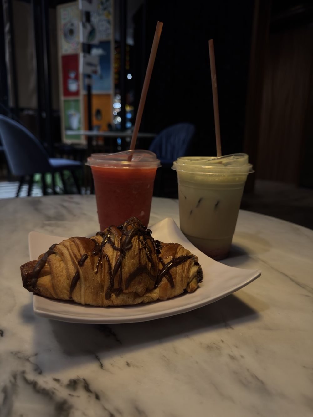 Café helado, frappé de fresa y croissant con chocolate sobre mesa de mármol